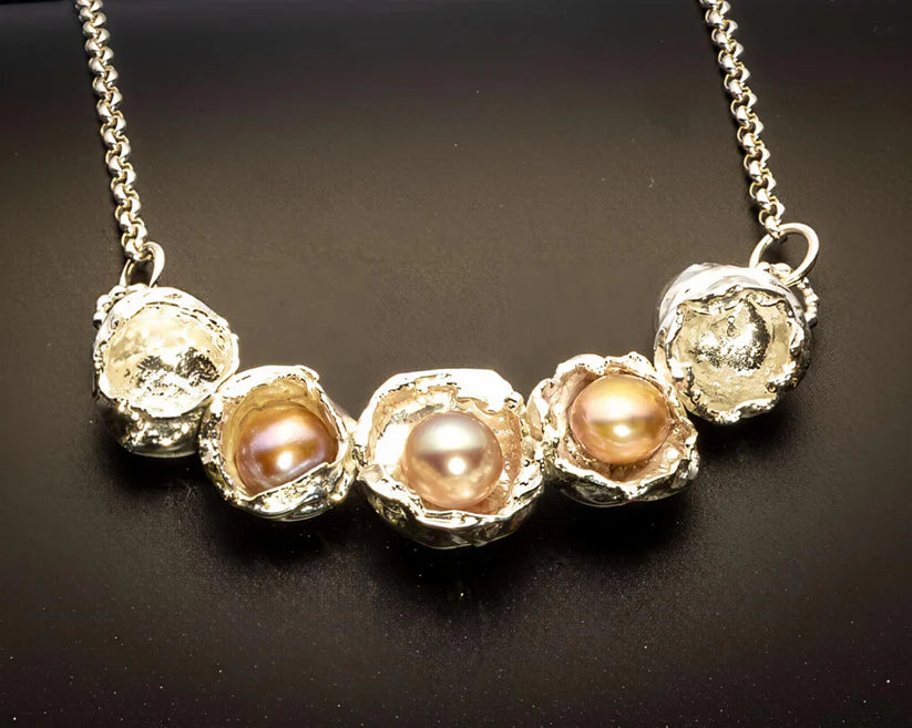 Necklace with pearls and textured metal elements on a dark background